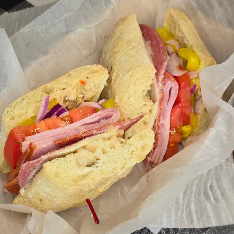 A Main St. Deli sandwich with ham, salami, cheese, tomatoes, onions, and peppers on a baguette.