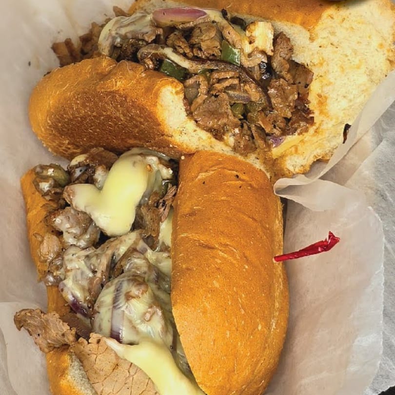 Two halves of a Main St. Deli cheesesteak sandwich, filled with steak, onions, and melted cheese.