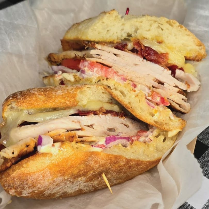 A Main St. Deli sandwich, cut in half, revealing turkey, cheese, bacon, tomato, and red onion.